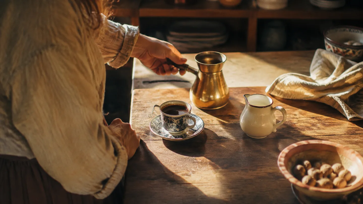 A small cezve and two dark coffee cups sit ready while a pitcher of milk remains untouched beside them.