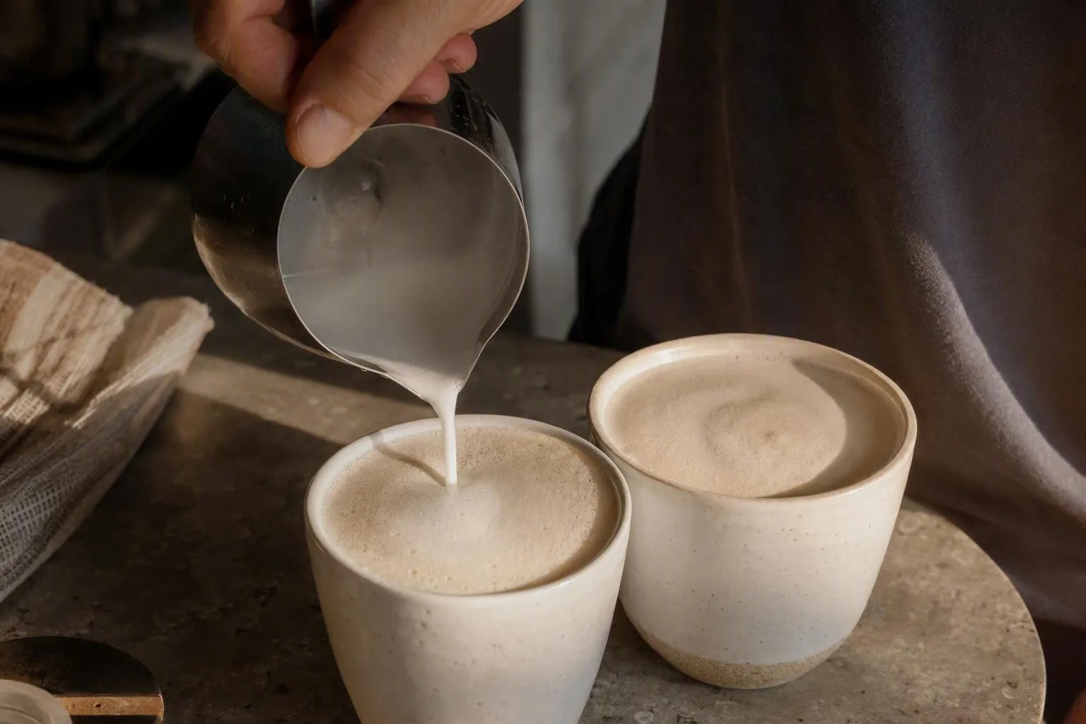 Glossy fine-bubbled milk pours into a small espresso drink beside a larger milk coffee for comparison.