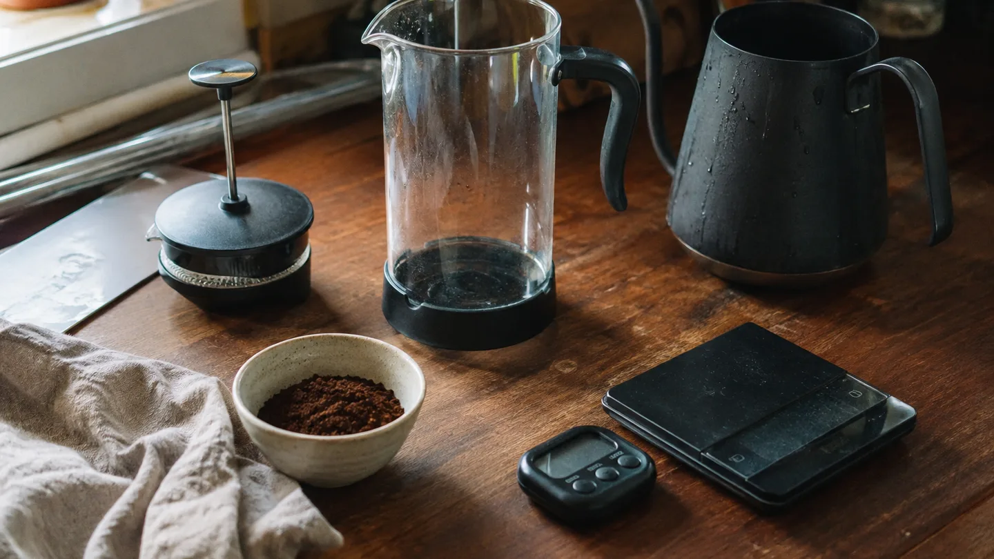 A French press, measured coffee grounds, water, scale, and timer are arranged for a repeatable brew.