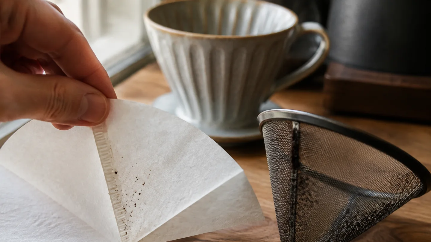 A paper filter and metal mesh sit beside a dripper, showing the dense and open structures that catch coffee grounds.