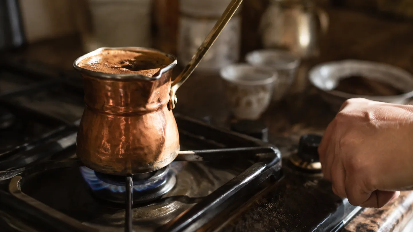 Foam gathers around the coffee surface as a hand keeps the burner on a low setting.